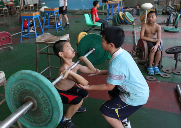 A boy practises with the help of experienced athletes at a weightlifting training base in Xiamen, Fujian province. Mo Feng / for China Daily Future Olympians
