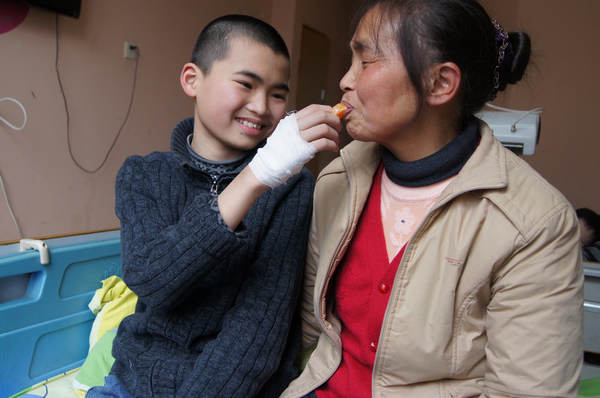 Thirteen-year-old Wan Chenchen feeds an orange to his grandmother Yang Debi, his only family member, at a hospital in Chongqing on Feb 22, as he prepares for an operation to remove an extra finger on his hand the next morning. Jin Ji / for China Daily Operation gives boy hope
