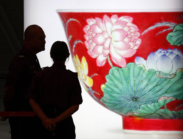 Security guards chat in front of a light box featuring a photograph of a magnificent Ruby-Ground Falangcai 'Double-Lotus' Bowl Blue Enamel Yuzhi Mark and Period of Kangxi at Sotheby's Spring Sales in Hong Kong April 8, 2013. New auction record set for Kangxi porcelain