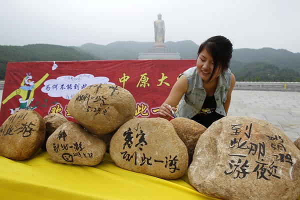 A woman leaves a message on a stone provided at the Zhongyuan Buddha tourist site, situated in Lushan county, Henan province, May 28, 2013. Graffiti allowed at Buddha statue