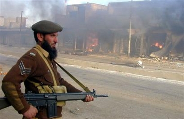 A soldier of the Pakistani paramilitary force stands guard near shops set on fire by an angry mob after a suicide bombing on a Shiite procession in Ustarzai near Hangu, Pakistan, Thursday, Feb. 9, 2006.