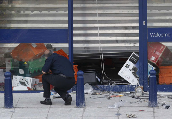 An employee looks into a damaged electrical shop which was attacked by looters overnight in Brixton, south London August 8, 2011.[ UK police arrest over 160 in weekend London riots