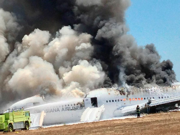 Asiana Airlines Boeing 777 is engulfed in smoke on the tarmac after a crash landing at San Francisco International Airport in California July 6, 2013, in this file handout photo provided by passenger Eugene Anthony Rah, released to Reuters on July 8, 2013. Asiana to sue TV station over pilot name gaffe