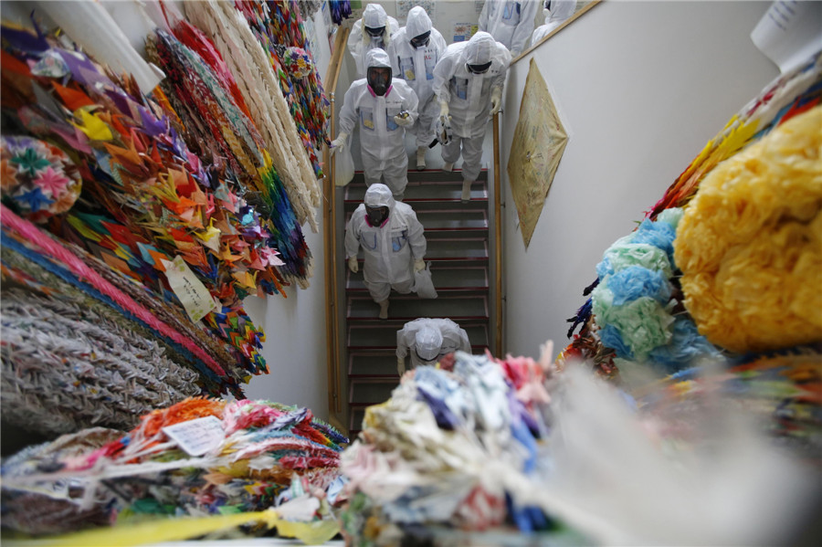 Members of the media and Tokyo Electric Power Co. (TEPCO) employees, wearing protective suits and masks, walk alongside a wall lined with thousands of paper cranes inside the main anti-earthquake building at the tsunami-crippled TEPCO's Fukushima Daiichi nuclear power plant in Fukushima prefecture March 10, 2014 Visit to Fukushima nuclear plant on meltdown anniversary